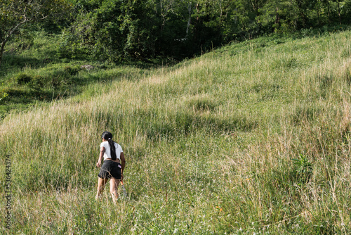 general shot of a latin peasant girl walking up a mountainside towards her home. young woman walking through a pasture in a farm located in Quinchia Colombia.