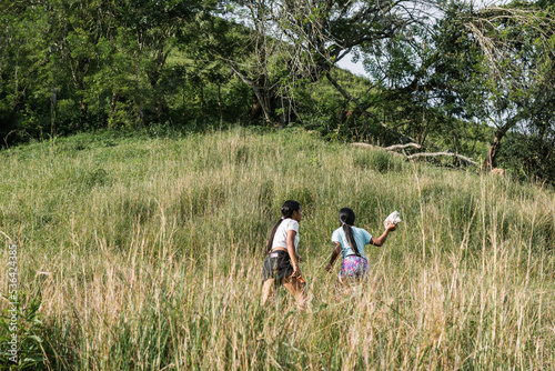 two peasant girls, brunette latinas walking down the side of a mountain, going to get firewood to make food. women walking a long way to get to their destination.