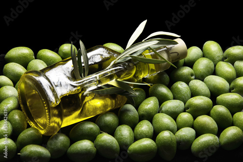 Bottiglia extra vergine d’oliva su un tappeto di olive verdi photo