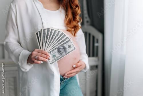pregnant woman holding money dollars, cost of giving birth and maternity needs, expensive medical treatment for women childbirth. selective focus