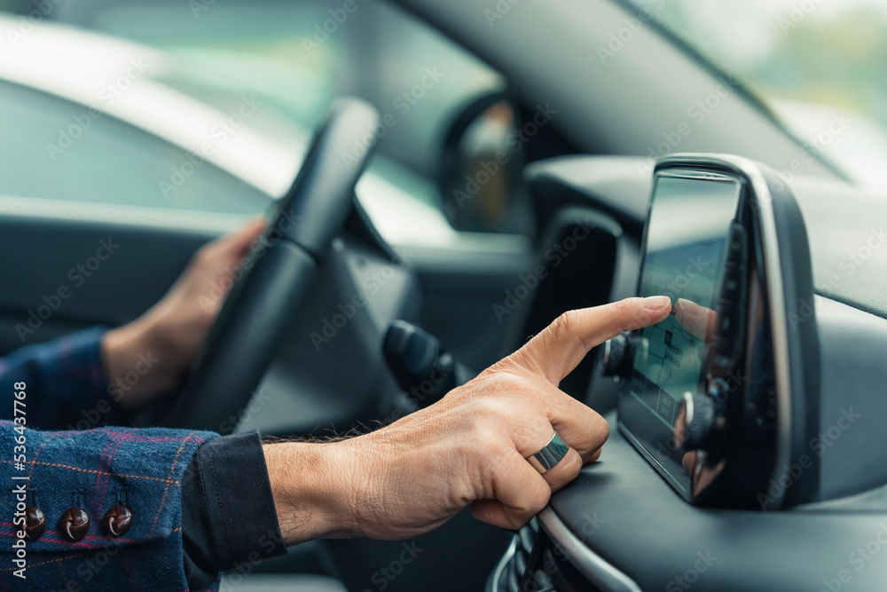 Car interior. Modern gadgets and facilitations for drivers. Closeup indoor shot of unrecognizable caucasian person clicking modern's car touch screen to change settings with one hand, and holding Car interior. Modern gadgets and facilitations for drivers. Closeup indoor shot of unrecognizable caucasian person clicking modern's car touch screen to change settings with one hand, and holding