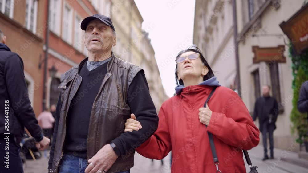 Elderly couple of tourists are walking through the historical center in an old European city. Palace Square, Warsaw Old Town Elderly couple of tourists are walking through the historical center in an old European city. Palace Square, Warsaw Old Town