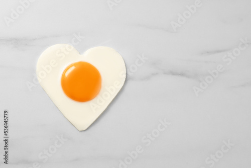 Heart shaped fried egg on white marble table, top view