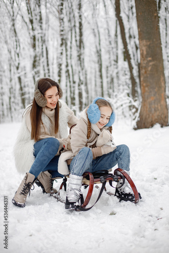 Brunette mother and and her daughter sitting on a sled in winter forest