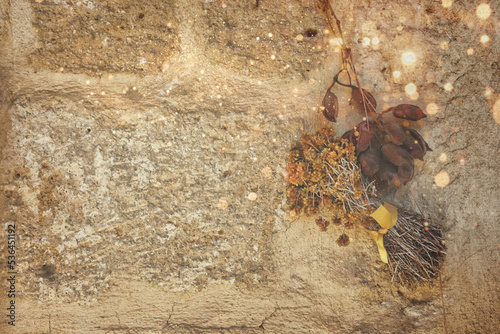 dried St. John's Wort, dried leaves and yellow light beams reflected on the wall, hanging on an old stone wall. Autumn wallpaper