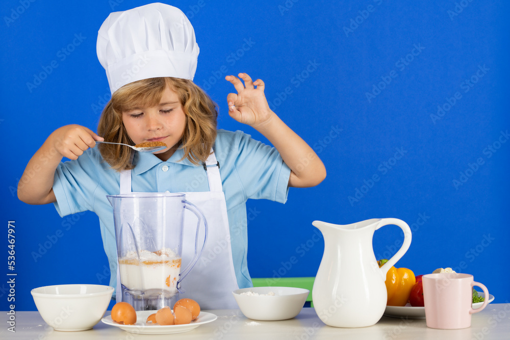 Kid boy in chef hat and apron cooking preparing meal. Little cook with vegetables at kitchen. Natural kids food. Kid boy in chef hat and apron cooking preparing meal. Little cook with vegetables at kitchen. Natural kids food.