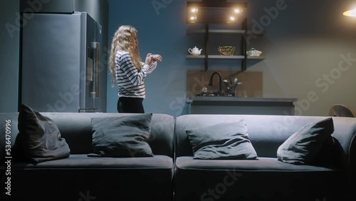 Woman enters kitchen, turns on lights with smart watch in her smart home IoT system. Female uses application on watch to control lightning scenarios in a living room, pouring wine. Internet of things.