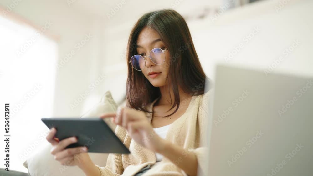 Young asian woman wearing glasses and using tablet while seated on couch at home Young asian woman wearing glasses and using tablet while seated on couch at home