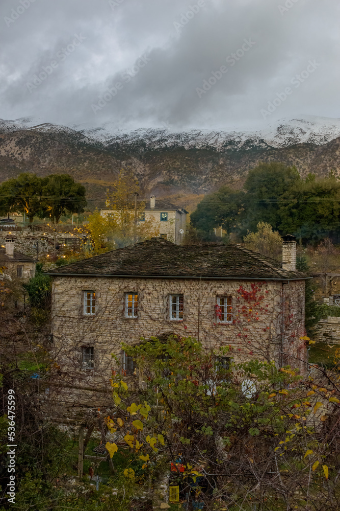 Τraditional architecture  with the stone buildings and snowy mountains as background during  fall season in the picturesque village of papigo , zagori Greece