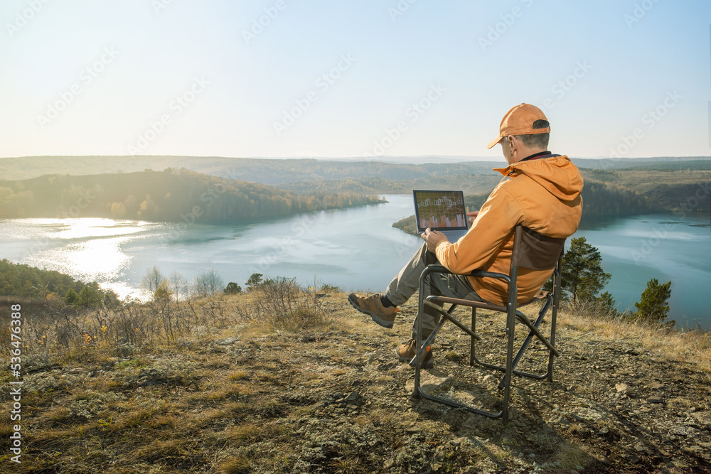Man using a laptop in the mountain at sunset. Remote work concept.