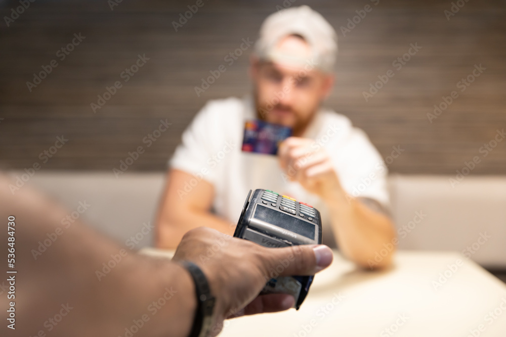 A young man is debating whether to use a credit card or cryptocurrency for payment. Card payment versus bitcoin.