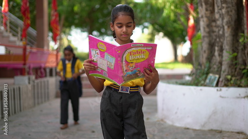 Cute and studious little Indianasian girl studyingreading book while standing