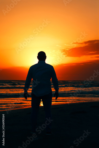 a silhouette of a man facing the sea at a beach during the sunset and focusing his mind on relaxation.