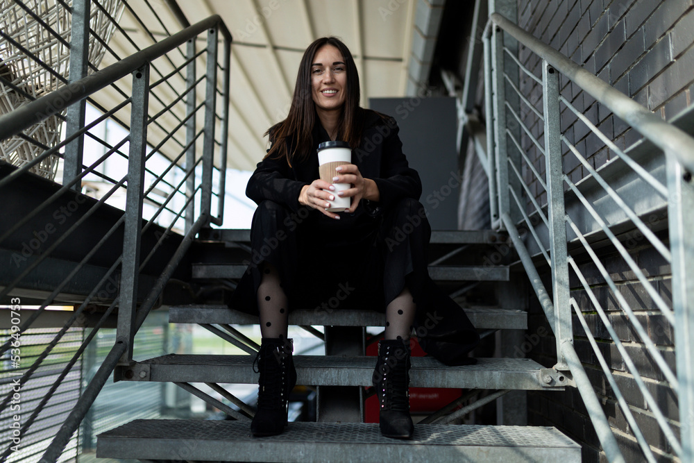 portrait of a successful modern stylish woman with a cup of coffee in her hands against the background of stairs in a modern building