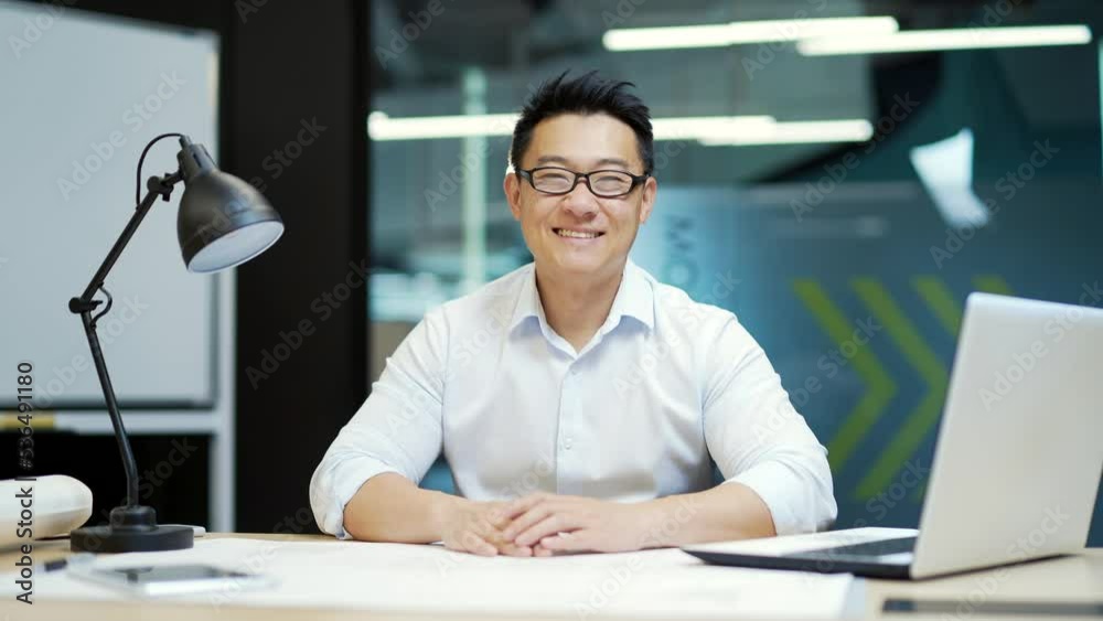 portrait of asian man engineer, designer architect looking at camera sitting at workplace in modern office. male employee worker in glasses is smiling. at a computer desk indoors portrait of asian man engineer, designer architect looking at camera sitting at workplace in modern office. male employee worker in glasses is smiling. at a computer desk indoors