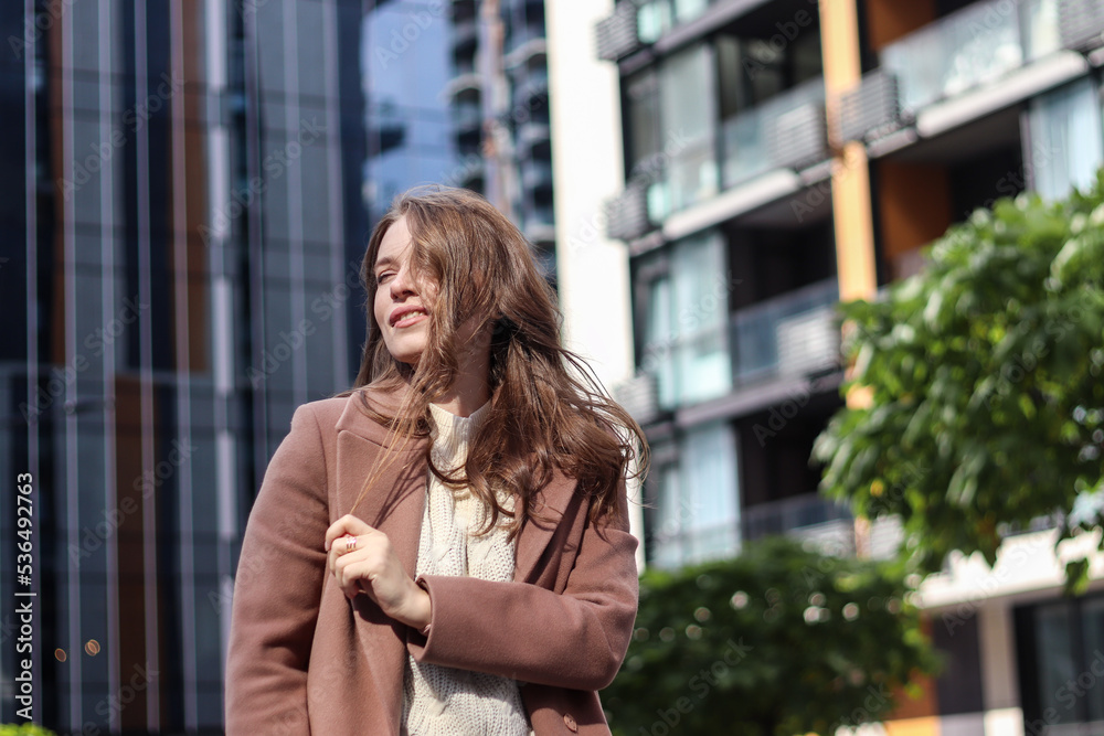 Street photo session of a girl with blond long hair in a beige coat. Photo shoot in the big city. Street photo session of a girl with blond long hair in a beige coat. Photo shoot in the big city.
