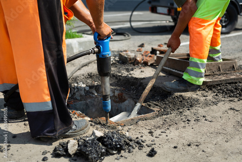 A road worker is dismantling street asphalt and old drainage with a jackhammer.