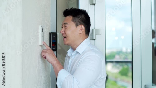 Asian man, calling rings the intercom of the house, pressing the button, waiting for the door to open. Male pushing the button and talking doorbell with camera near entrence electronic code lock photo