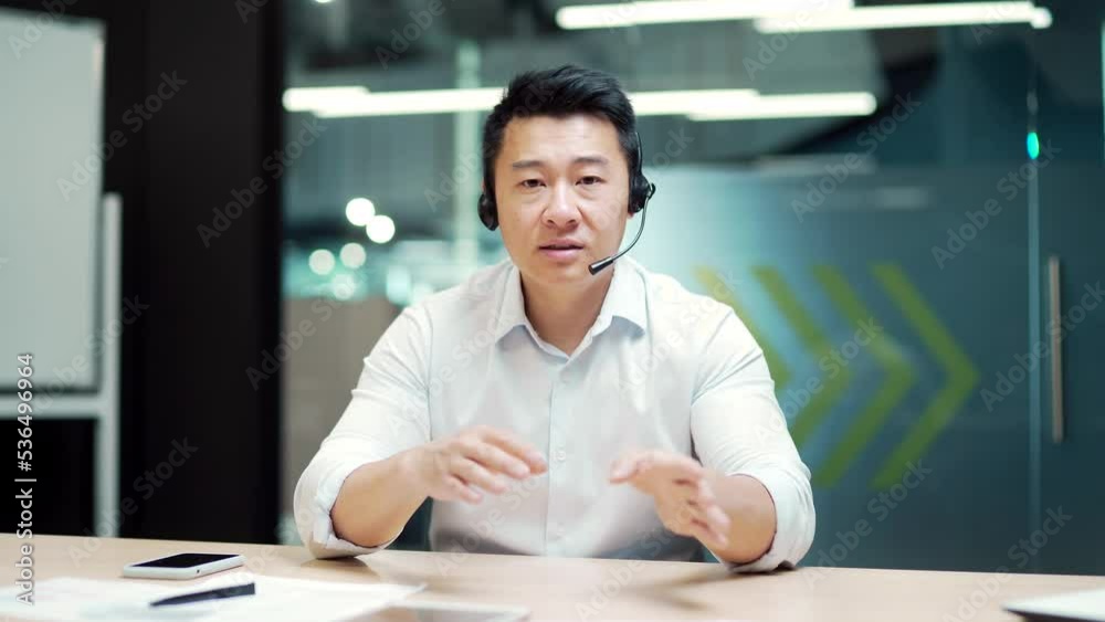 Asian business man manager holds online meeting conference remotely by video call using a webcam, headset. Office worker office with laptop computer. Talk look at camera view