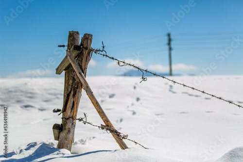 Der Pfahl eines selbstgebauten Holzzauns mit Stacheldraht ragt aus dem verschneiten Boden heraus photo