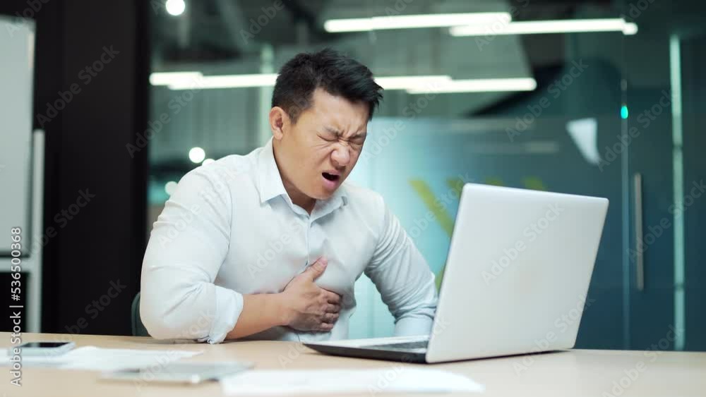 Asian business Man employee with a heart attack office worker with severe heart pain. holding chest . male businessman Sitting at work a computer desk. manager suffers in Workplace. Indoor. Asia Asian business Man employee with a heart attack office worker with severe heart pain. holding chest . male businessman Sitting at work a computer desk. manager suffers in Workplace. Indoor. Asia