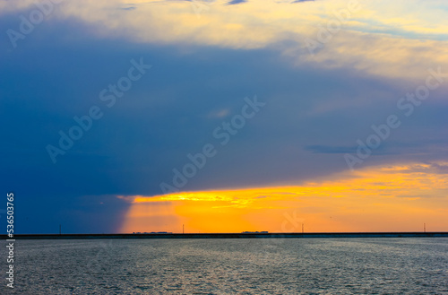 A storm at sea. A blue rain cloud hung in the sky over the blue sea at sunset in the evening. The orange-blue sky. An ocean  a river  a body of water. A breakwater on the horizon. Calm stormy skyline.