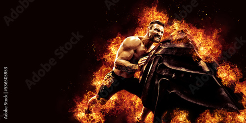 Muscular fitness shirtless man moving large tire in flames, concept lifting, workout cross training