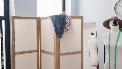 Young beautiful hispanic woman taking off clothes on fitting room at clothing factory