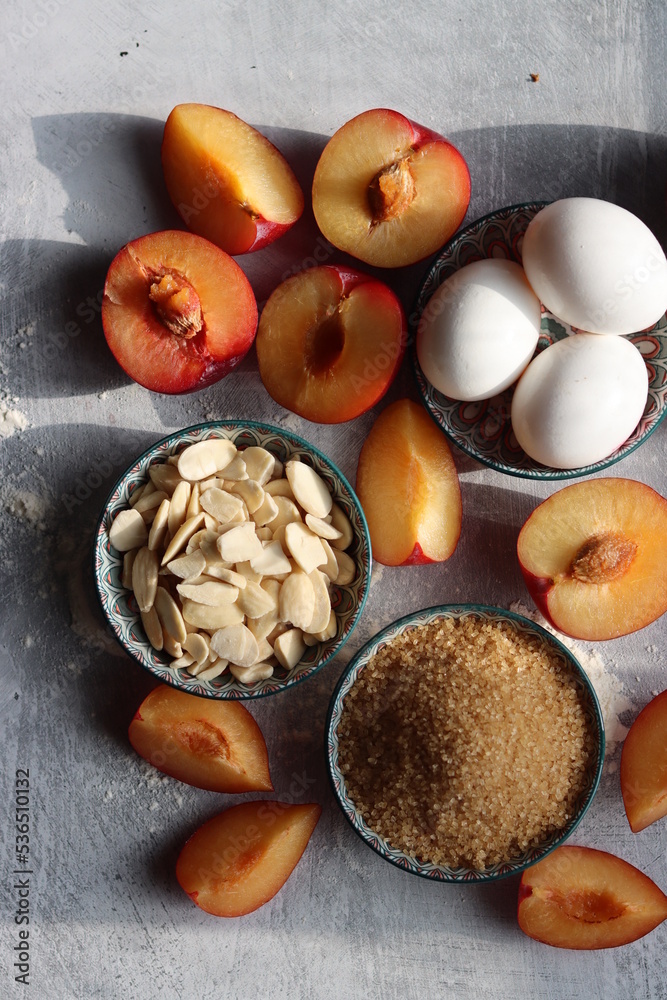 Plum pie in process. Fresh ingredients on a table. Top view photo of plums, almonds, demerara sugar, eggs. Sweet cake ingredients closes up. 