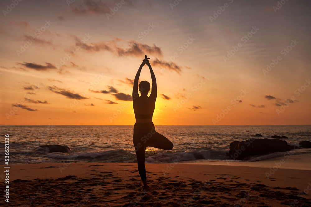 Silhouette slim woman does asana yoga position arms raised on tropical sea coast sandy beach outdoors at sunset. Female performs exercises for healthy lifestyle to restore strength, spirit. Copy space