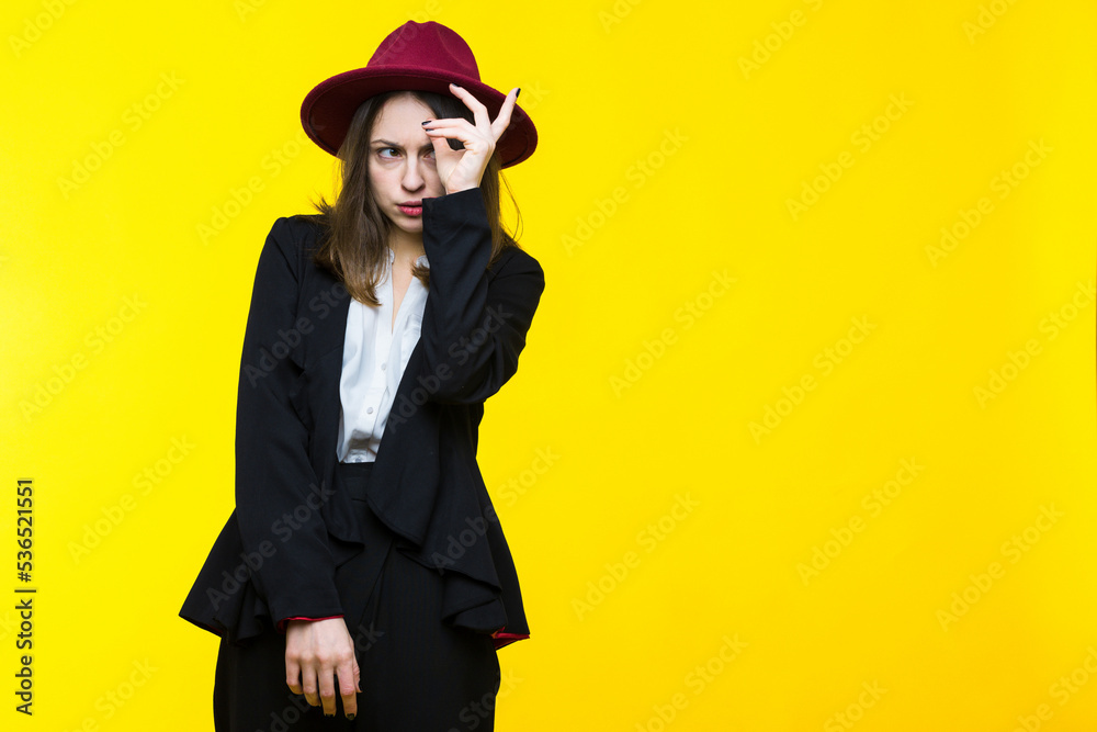 Fototapeta premium Brunette in a suit and hat on a yellow background.