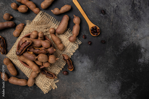 Tropical fruits, Tamarindo beans in shell on a brown butchers block on a dark background, healthy fruit. Long banner format. top view photo