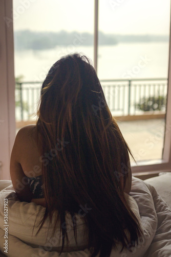 Free Download a woman looking out window sitting on her cozy bed - GFXLoad