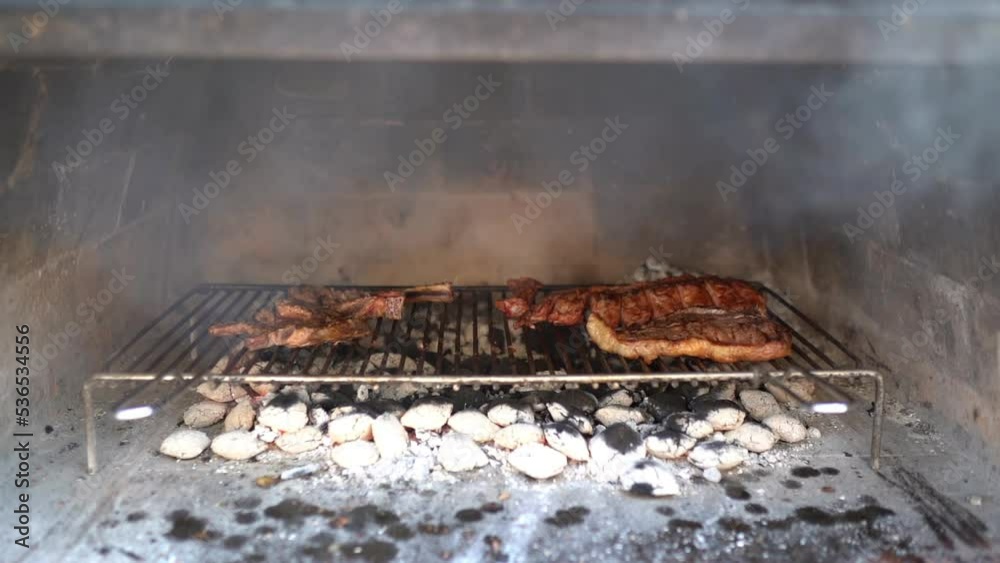 Meat ribs and steaks roasting on burning charcoal fire, preparation of roasted meat for bbq party, meat assortment in smoker, barbecue concept Meat ribs and steaks roasting on burning charcoal fire, preparation of roasted meat for bbq party, meat assortment in smoker, barbecue concept