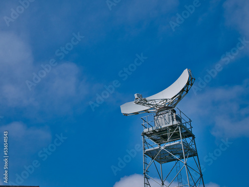 A white radar dish mounted on a steel frame tower. Taken on a sunny day in Summer.
