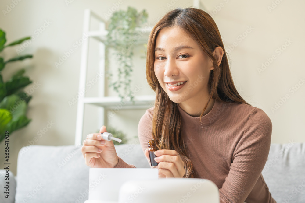 Happy asian young woman, girl hand holding bottle of essential and drop oil into air humidifier, enjoy aromatherapy steam scent diffuser comfortable while rest in living room, apartment at home. Happy asian young woman, girl hand holding bottle of essential and drop oil into air humidifier, enjoy aromatherapy steam scent diffuser comfortable while rest in living room, apartment at home.