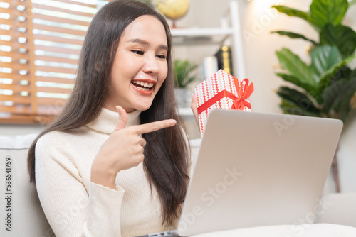 Celebrate on day of happy birthday season, pretty asian young woman using laptop computer, greeting on video call during social distance, holding gift box, happy to get present on couch, sofa at home.