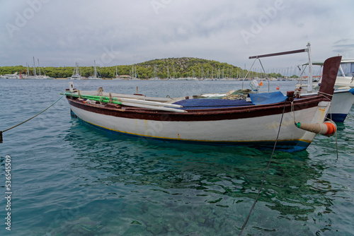 White fishing boat for rowing in the beautiful blue crystal clear waters of the Croatian Mediterranean. In the background there is a marina and green mountains. © Stefan
