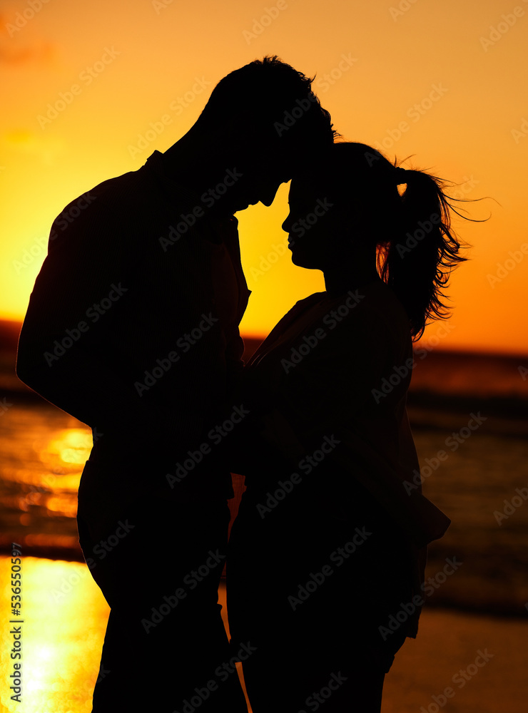 Silhouette of young couple on the beach at sunset embracing each other in affection. People on holiday, vacation and honeymoon by the ocean. Intimate, love and romantic man and woman together by sea