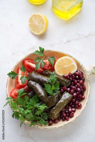 Dolmades with pomegranate, fresh parsley, tomatoes and lemon, vertical shot on a light-beige marble background