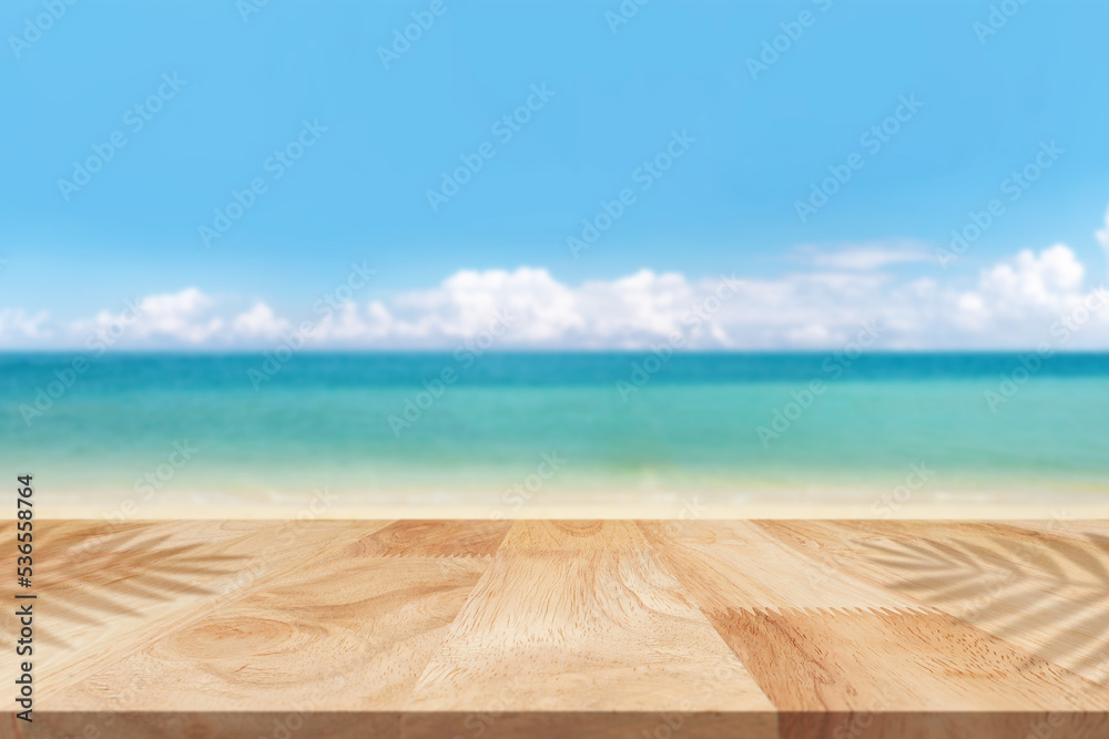 Empty wooden tabletop with leaf shadow against scenic view of beach. For your product placement to the table top in the foreground