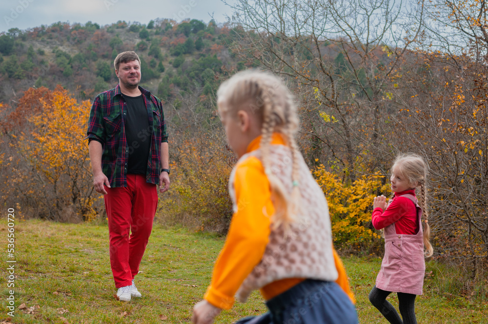 dad has fun playing catch-up with his little twin daughters in an autumn meadow on a warm day