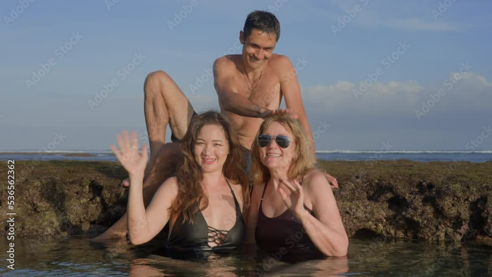Happy family at summer vacation bathing in ocean reef pool and swimming in salty water at sunset. Elderly mother and adult children having fun and waving to camera on beach at seaside. Slow motion. Happy family at summer vacation bathing in ocean reef pool and swimming in salty water at sunset. Elderly mother and adult children having fun and waving to camera on beach at seaside. Slow motion.