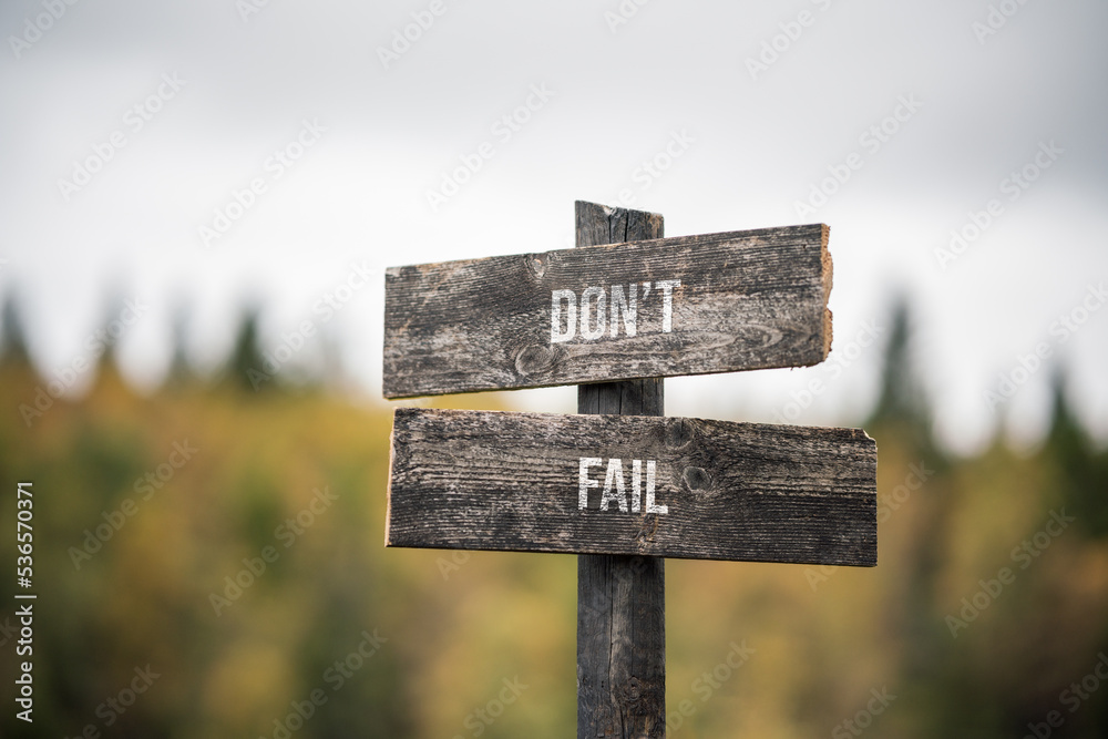 vintage and rustic wooden signpost with the weathered text quote dont fail, outdoors in nature. blurred out forest fall colors in the background.