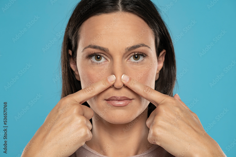 Portrait of young woman touches her nose on a blue studio background Portrait of young woman touches her nose on a blue studio background