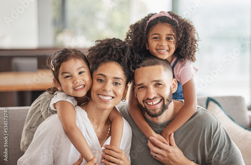 Happy, smile and portrait of an interracial family sitting on a sofa in the living room at home. Happiness, love and adoptive parents bonding, embracing and relaxing with their children in the lounge