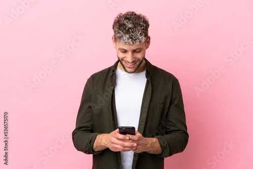 Young handsome caucasian man isolated on pink background sending a message with the mobile