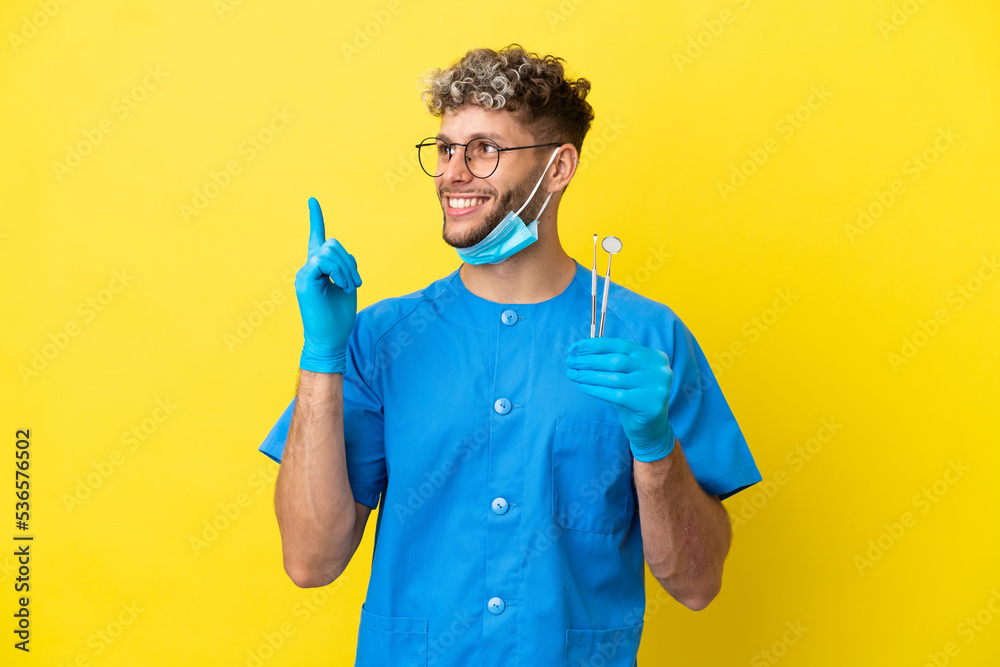 Dentist caucasian man holding tools isolated on yellow background pointing up a great idea Dentist caucasian man holding tools isolated on yellow background pointing up a great idea