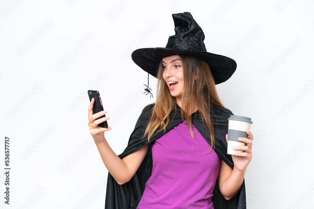 Young caucasian woman costume as witch isolated on white background holding coffee to take away and a mobile Young caucasian woman costume as witch isolated on white background holding coffee to take away and a mobile