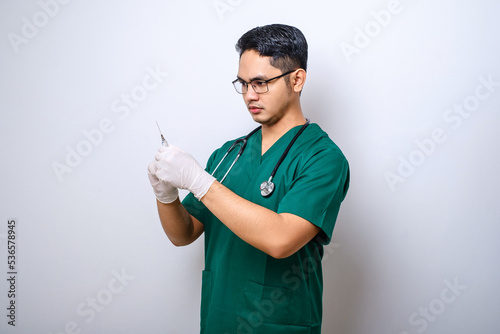 Potrait of asian male doctor, wearing green scrubs and gloves, fill syringe with vaccine, doing vaccination shots